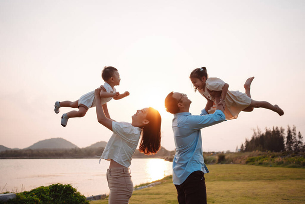 Happy family in the park sunset light. family on weekend playing together in the meadow with river Parents hold the child and daughter hands.health life insurance plan concept. - Photo, image