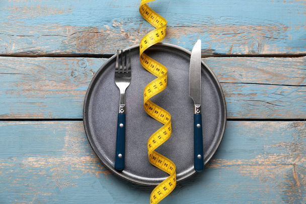 Yellow measuring tape, plate and cutlery on blue wooden background - Φωτογραφία, εικόνα