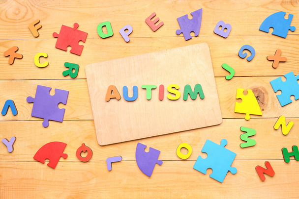 Word AUTISM with letters and puzzle pieces on wooden background - Photo, Image