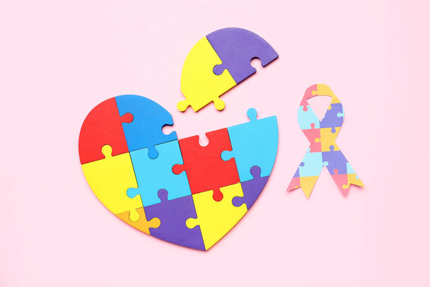 ピンクの背景にパズルピースで作られたハートの紙リボン。世界自閉症啓発デー - 写真・画像