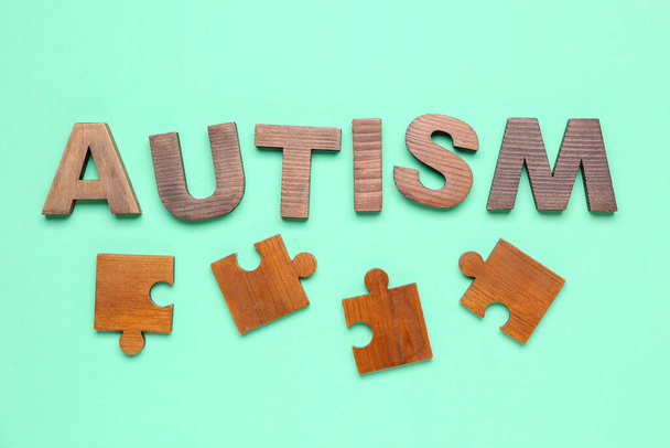Word AUTISM with puzzle pieces on green background - Фото, зображення