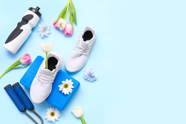 Sneakers con attrezzature sportive e fiori primaverili su sfondo blu - Foto, immagini