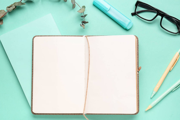 Composition with blank notebook, glasses and pens on turquoise background - Photo, Image