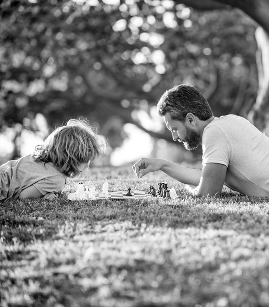 father and son playing chess on green grass. fathers day. happy family. parenthood and childhood. checkmate. spending time together. strategic and tactic. tutorship. dad and kid play logic game. - Foto, Imagen