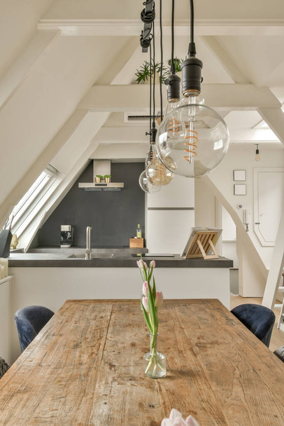 ένα ξύλινο τραπέζι και καρέκλες σε ένα δωμάτιο με μια σοφίτα στυλ οροφής από πάνω του, υπάρχει μια λάμπα κρέμεται πάνω από την κορυφή - Φωτογραφία, εικόνα