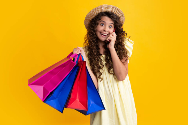 Beautiful fashion teenager child girl with shopping bags on yellow background. Shopaholic shopping and fashion. Kid with shopping sale bags. Happy teenager, positive and smiling emotions - Photo, Image