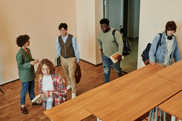 Opettaja smart casualwear seisoo edessä avoin ovi ja kokous ryhmä opiskelijoita tulee tilava luentosali ennen oppituntia - Valokuva, kuva