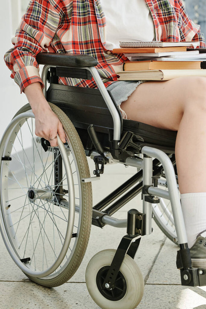 Женский зумер в белой футболке и клетчатой рубашке вращающиеся колеса инвалидного кресла при движении по коридору колледжа или университета - Фото, изображение