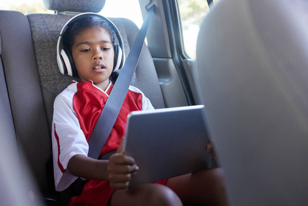 Sports, car travel and relax child with tablet on journey to soccer practice while streaming video, watch movie or play online games. Transport, SUV van or kid girl using tech before football match. - Photo, Image
