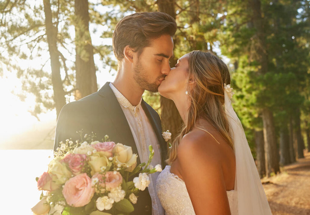 結婚式、結婚式、公園での夫婦のキス、愛、ケア、結婚へのコミットメントを祝うための森と自然。花嫁、新郎、庭園でのロマンス、ブライダルイベントやお祝いの儀式のキス. - 写真・画像
