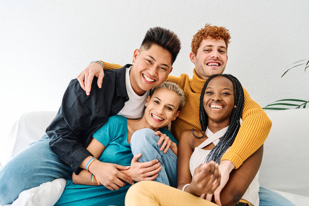 Retrato de um grupo multiétnico de amigos abraçando o sofá enquanto olha para a câmera e sorri - Foto, Imagem