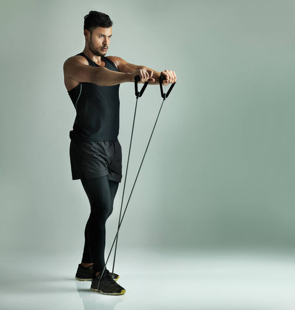 Staying in top form with resistance training. Studio shot of a young man working out with a resistance band against a gray background - Фото, изображение