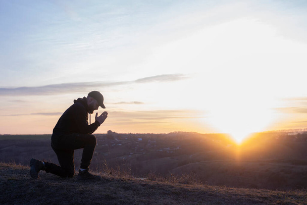 Gebed. Man op zijn knieën biddend. Tegen de achtergrond van de lucht en zonsondergang. Vergeving van zonden en berouw. Pasen - Foto, afbeelding