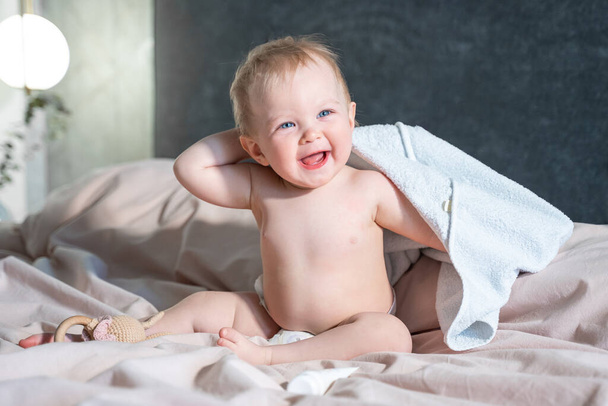 Baby in bath towel after hygiene procedures, lying on parent bed in bedroom. Hold comb Hygiene and skin care for children. Laughing smiling - Photo, Image