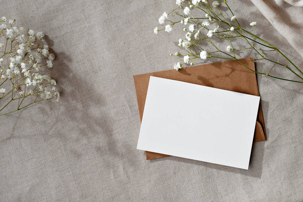 Элегантный пастельный бизнес, шаблон бренда, чистая бумажная карточка с макетом копировального пространства, конверт и цветы на нейтральном бежевом фоне - Фото, изображение