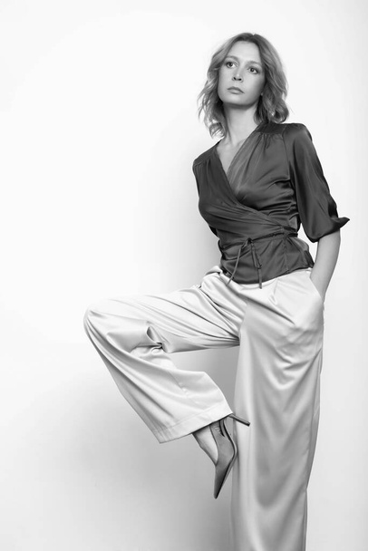 Zwart-wit modeportret van jong vrouwelijk model met zijden satijnen wrap blouse en wijde broeken. - Foto, afbeelding