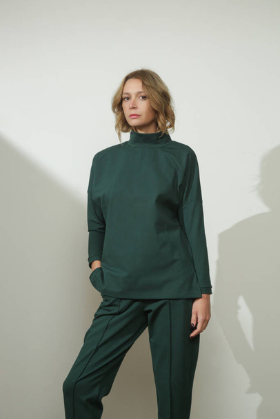 Fiatal női modell stúdióképeinek sorozata zöld színű alapvető garbót és magas derékú cigarettanadrágot visel  - Fotó, kép