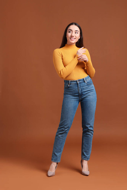 Young woman in stylish jeans on brown background - Φωτογραφία, εικόνα