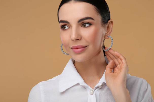 Beautiful young woman with elegant earrings on beige background - Zdjęcie, obraz