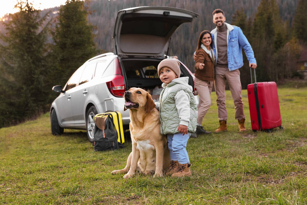 Dog, cute little girl and her parents near car in mountains. Family traveling with pet - Photo, Image
