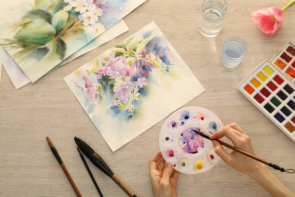 Woman painting flowers with watercolor at white wooden table, top view. Creative artwork - Foto, immagini