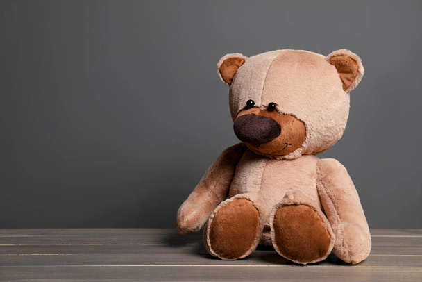 Cute teddy bear on wooden table near black wall, space for text - Photo, Image