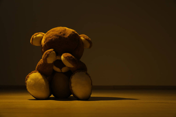 Cute lonely teddy bear on floor in dark room. Space for text - Фото, изображение