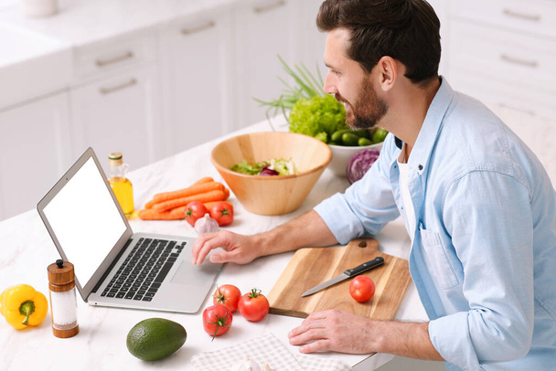 Man making dinner while watching online cooking course via laptop in kitchen - 写真・画像