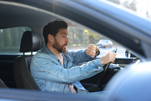 Emotional man checking time on watch in car. Being late concept - Photo, Image