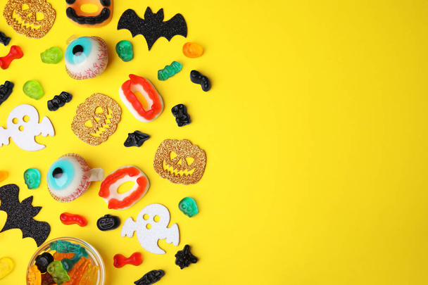 Tasty candies and Halloween decorations on yellow background, flat lay. Space for text - Foto, afbeelding