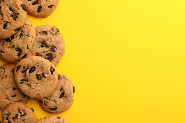 Many delicious chocolate chip cookies on yellow background, flat lay. Space for text - Фото, изображение