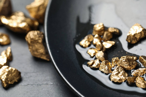 Plate with gold nuggets on black table, closeup - Φωτογραφία, εικόνα