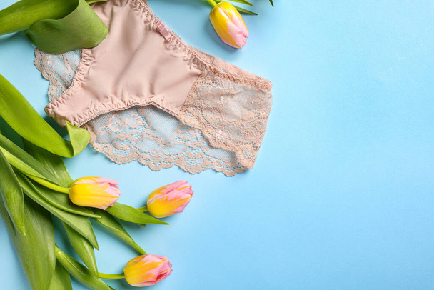 Elegant beige women's underwear and beautiful tulips on light blue background, flat lay. Space for text - Foto, imagen