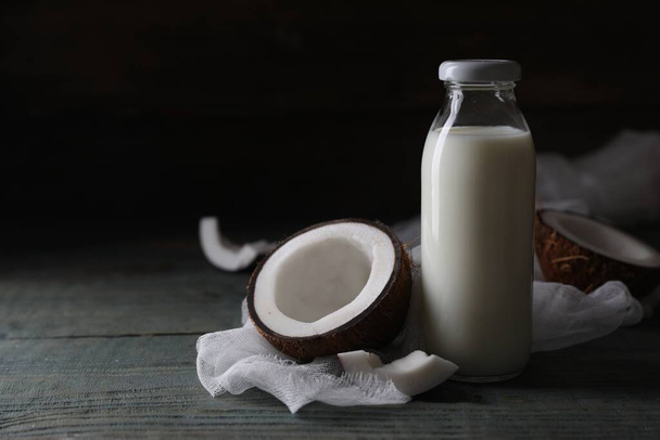 Bottle of coconut milk and nut on wooden table, space for text - Фото, зображення
