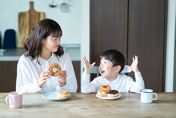 母親と息子は家でドーナツを食べて - 写真・画像