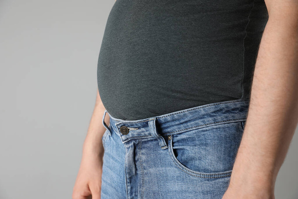 Overweight man in tight tshirt and jeans on light grey background, closeup. Space for text - Foto, imagen