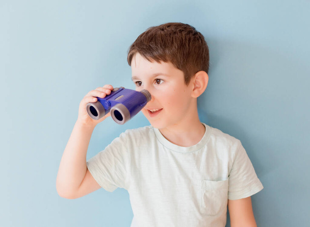 Caucasian boy with toy binoculars on a blue background with copy space. Travel funny concept - Zdjęcie, obraz