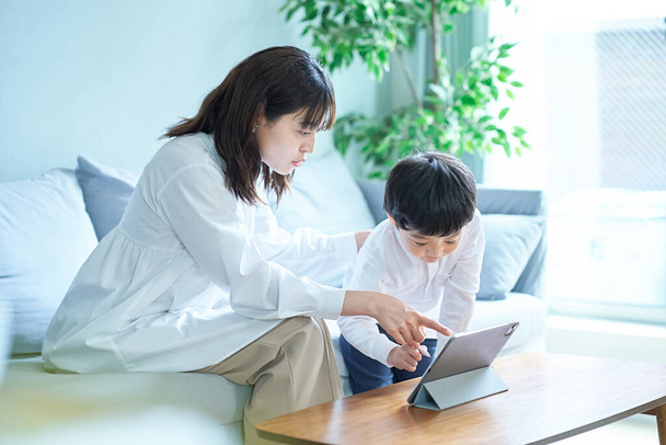 Мать и ребенок сидят на диване и смотрят на экран планшетного ПК - Фото, изображение