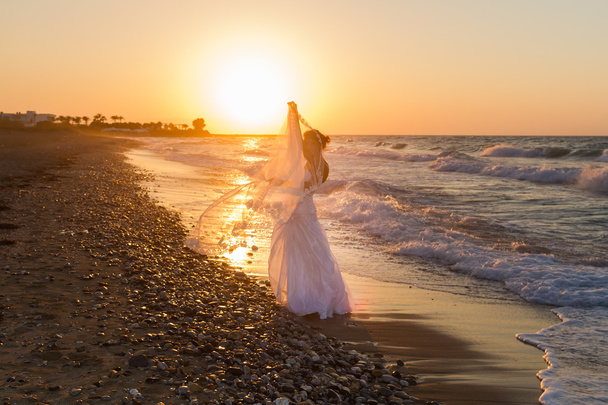 Young bride enjoys walking on a hazy beach at dusk. - Фото, изображение