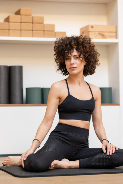 Peaceful beautiful female in activewear sitting on mat and resting during yoga session while looking at camera - Foto, Imagen