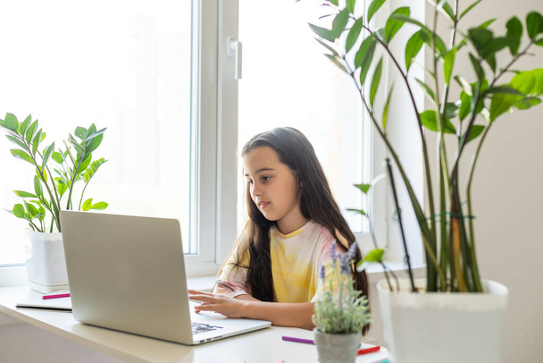 肯定的な子供の女の子の研究の写真リモートデスクテーブル使用ノートパソコンは、屋内家の中で家庭教師の書き込みレポートとオンライン通信レッスンを持っています - 写真・画像