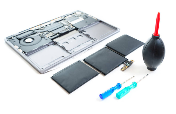 Swollen laptop battery placed next to a disassembled laptop, along with screwdrivers and an air blower for cleaning dust from the components. Essential battery replacement set. - Photo, Image