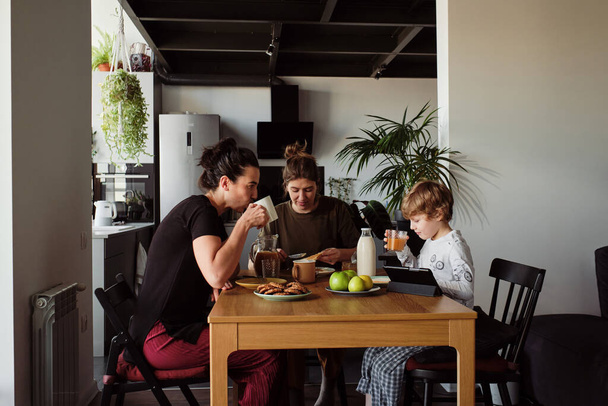 Familia de dos jóvenes con niño sentado a la mesa y desayunando en la cocina - Foto, imagen