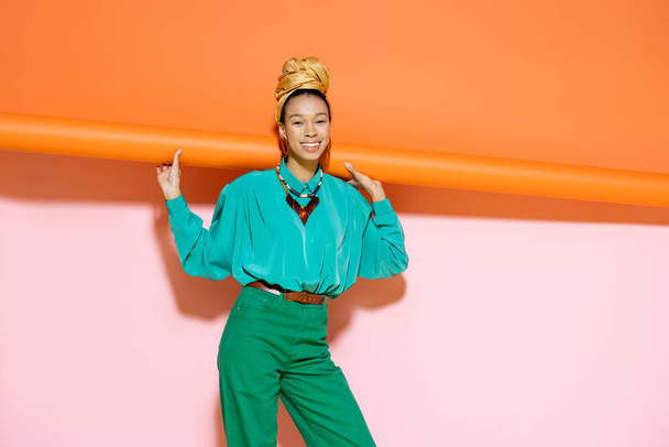 Smiling african american woman in bright outfit posing on colorful background  - Zdjęcie, obraz
