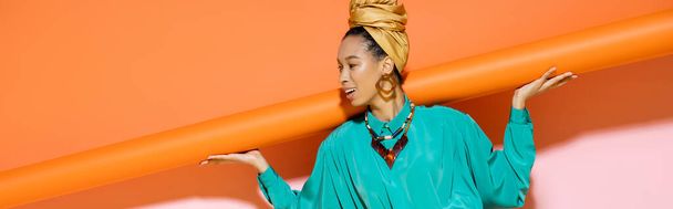 Carefree african american model with headscarf holding orange background, banner  - 写真・画像