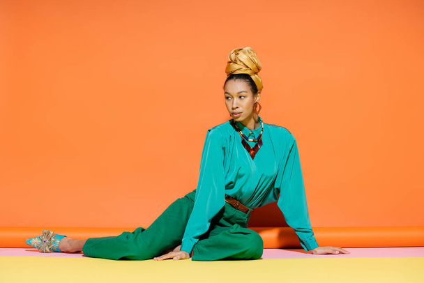 Stylish african american woman in headscarf and bright blouse sitting on colorful background  - Foto, Bild