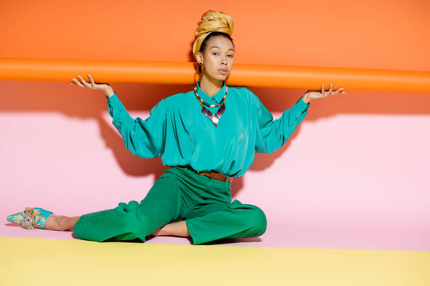 Modelo afroamericano joven de moda en traje de verano sentado sobre un fondo colorido  - Foto, Imagen