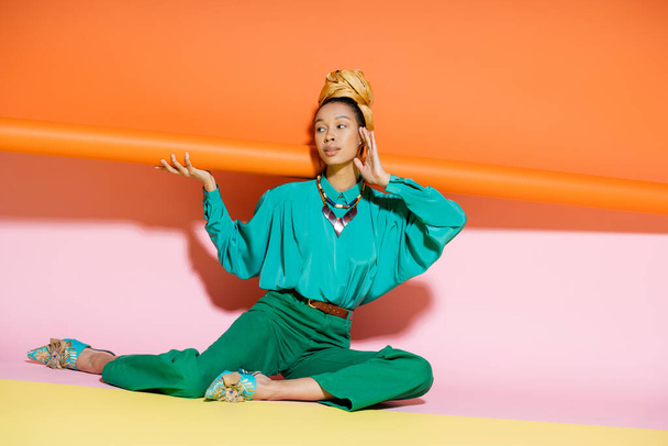 Fashionable african american woman in headscarf and bright outfit touching face on colorful background  - Φωτογραφία, εικόνα