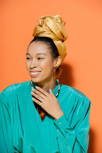 Portrait of cheerful african american model in headscarf looking away on orange background  - Photo, Image