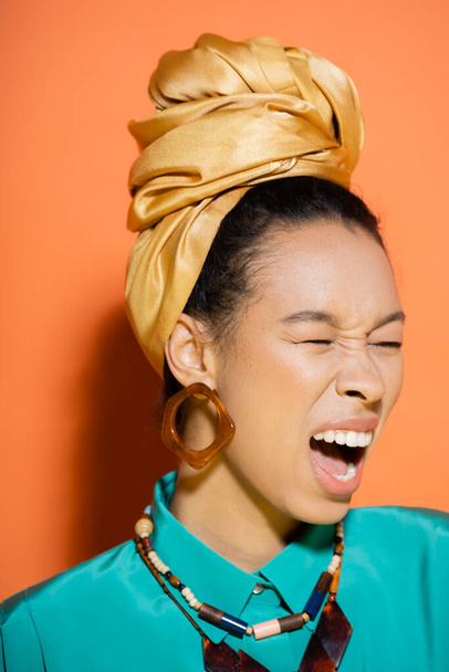 Stylish african american woman with headscarf screaming on orange background  - Fotó, kép